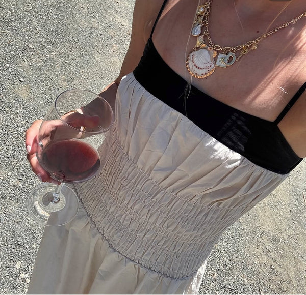 Customer in a cream dress wearing layered gold charm necklaces