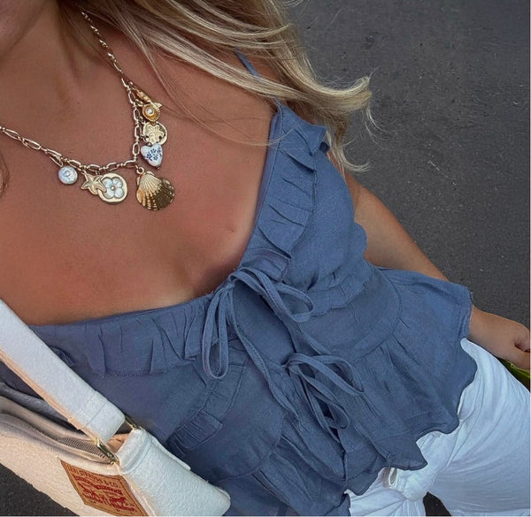 Close-up of a gold charm necklace with shell and enamel charms over a blue ruffled top