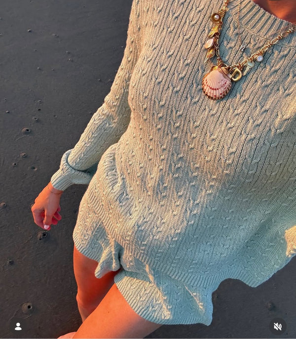 Close-up of a pink shell pendant charm necklace over a blue knit sweater on the beach